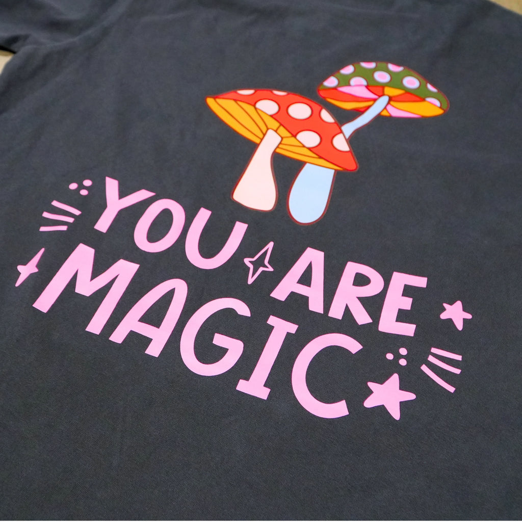 Happily berserk vintage black t shirt featuring a colorful graphic of two smiling mushrooms above the text 'YOU ARE MAGIC' in light pink, decorated with small stars and sparkles.
