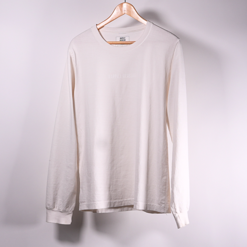 A long-sleeve happily berserk crewneck t-shirt in vintage white, hanging on a wooden hanger against a plain light  wall.